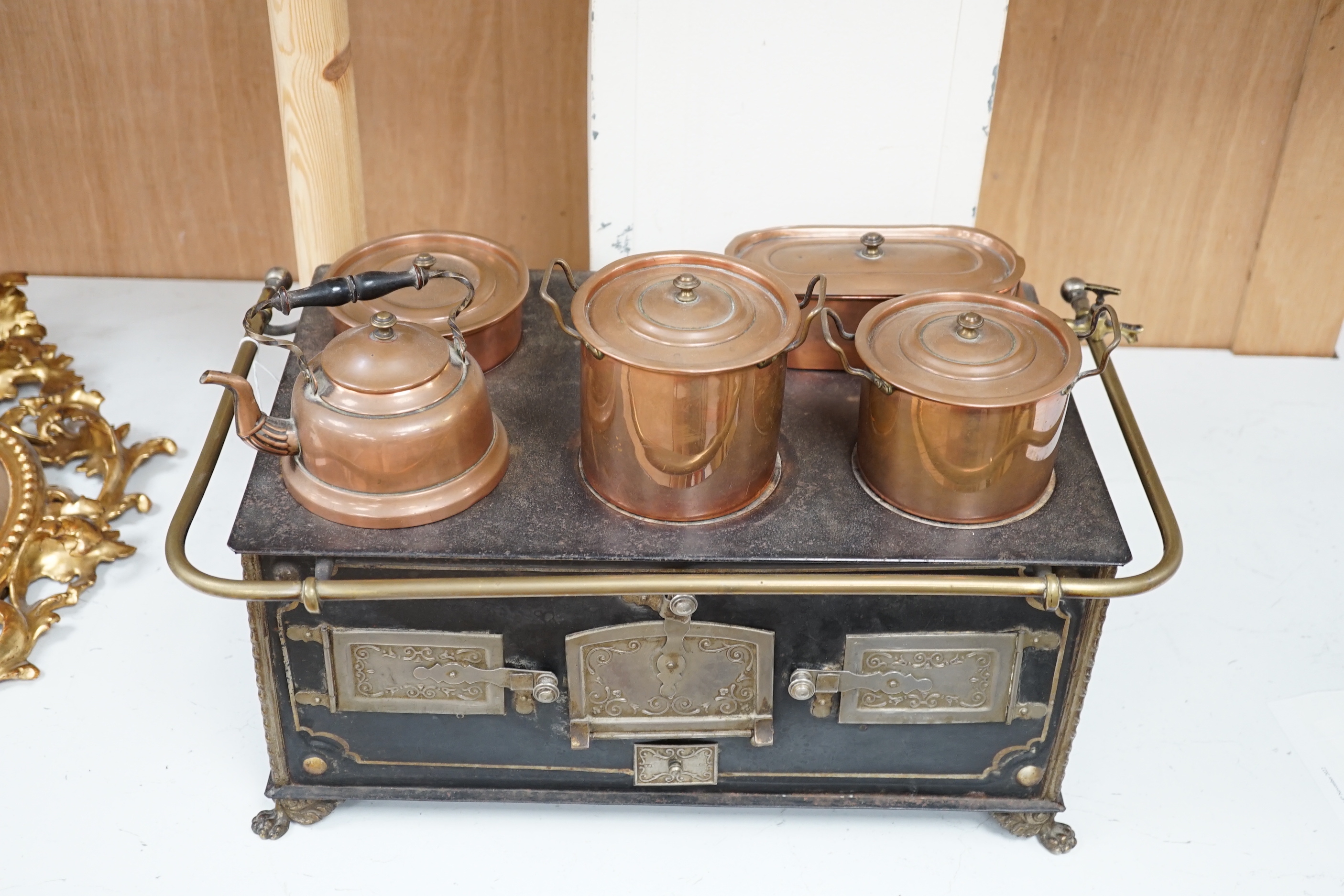 A Continental iron child's toy range/ stove, with a collection of copper fitted pans and a similar kettle, range 46cm wide x 28cm deep x 18.5cm high